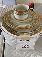 Photo of stacked Mikasa fine china including cup, saucer, salad plate, and dinner plate showing floral and gold decorative pattern.
