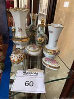 Porcelain set of two vases, three trinket boxes, and one decorative bottle arranged on a glass shelf with mirrored back.