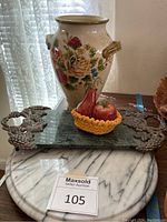 Photo showing the marble lazy susan underneath the granite serving tray with decorative metal grape handles, ceramic salt and pepper shakers in the yellow basket, and the large floral ceramic vase behind them.