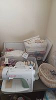 Singer Simple sewing machine on table with sewing supplies and baskets behind
