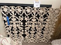 White vintage fireplace grate with floral vine design shown as three interlocking pieces with distressed white paint finish.