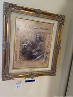 Full view of the framed art hanging on wall showing ornate golden frame and art print.