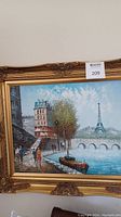 Full view of framed painting showing city walk scene with Eiffel Tower and boat on river.