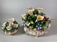 Two porcelain floral bouquets shown side by side on a flat surface, highlighting size difference and detailing.