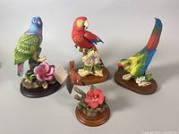 Four vintage bird sculptures on wooden bases displayed together on white background.