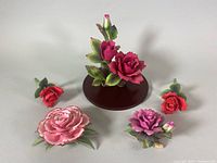 Group photo showing all five pink and red china flowers by Sadek, arranged on white background including display base for tallest rose.