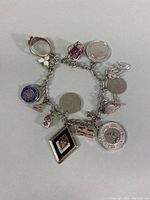 Full view of 7 inch sterling silver charm bracelet with 16 assorted charms, including New York Empire State, Florida license plate, graduation, crown, and other novelty charms.