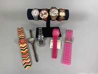 Full lot of 9 assorted watches displayed on stand and flat surface, showing variety of styles and bands.