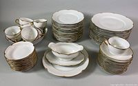 Full set with stacked plates, bowls, cups, saucers, serving bowl, and gravy boat with under-plate, all white with gold trim.