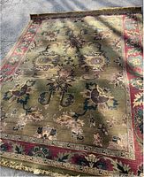 Full view of large wool area rug featuring green floral pattern with red border
