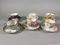 Front view of all three teacup and saucer sets arranged in two rows showing floral designs and gold accents.