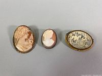 Three cameo brooches and pendant with detailed carving and metal settings on neutral background
