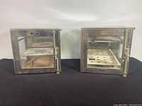 Front view of the pair of stainless steel and glass desiccators showing the shelves inside and BOEKEL nameplates.