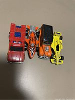 Top-down photo of four Hot Wheels die-cast cars: a red truck, orange flame car, orange vintage car, and yellow race car.