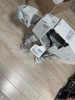 Side view of large grey plastic AT-AT Walker toy showing detailed paneling, articulated legs, and missing panels on main body.
