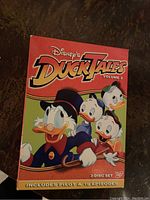 Red DVD box set with Disney's DuckTales Volume 2 branding and characters Scrooge McDuck, Huey, Dewey, and Louie, showing 3-disc set with pilot and 19 episodes included.