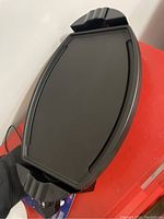 Black electric griddle with cooking surface and handles viewed on a red surface