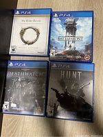 Four PlayStation 4 game cases on a wooden floor surface: The Elder Scrolls Online, Star Wars Battlefront, Warhammer 40,000: Deathwatch, and Hunt: Showdown.