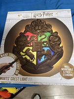 Boxed product showing the Harry Potter Hogwarts house crest with light up function activated by wand turn, indicating wall mountable and free standing options.