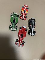 Four Hot Wheels Formula One racing cars in green, red, black-white, and red-orange colors viewed from above on a plain surface.