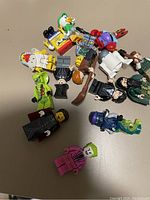 Photo showing a collection of 14 assorted Lego figurines from various franchises including Harry Potter, SpongeBob SquarePants, DC Comics, and Disney characters. Some figurines hold accessories like wands and weapons.