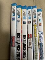 Photo showing six Wii U game cases stacked vertically, spine labels readable, including Just Dance 2015, Just Dance 2016, ESPN, LEGO The Hobbit, Pac-Man and the Ghostly Adventures, and 36 Best Games Obstacle Course.