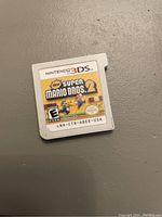 Photo of New Super Mario Bros. 2 game cartridge for Nintendo 3DS, front label visible, placed on a gray surface.