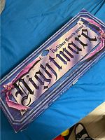 Top view of Nightmare The Video Boardgame box showing title and decorative border in purple and pink hues.