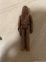 Close-up photo of a vintage Chewbacca figure showing brown plastic with sculpted fur, blue painted eyes, and a bandolier sash.