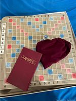 Scrabble gameboard laid flat with tile storage box and tile pouch on top