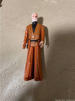 Full view of the vintage Obi-Wan Kenobi action figure standing upright on a textured surface, showing details of the figure's sculpt and paint.
