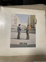 Photo of Pink Floyd Wish You Were Here vinyl album cover showing two men shaking hands, one on fire, set in an industrial backlot.