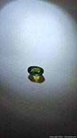 Photo of a single bright green oval cut sapphire gemstone on white background with shadow visible