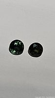 Photo showing two round green sapphire gemstones on white background, highlighting their color and faceting.