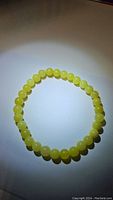 Top-down photo of natural lemon jade bracelet showing round yellow-green beads on a stretchy band, placed on a white surface under light.
