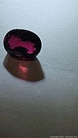 Oval cut deep dark red-purple rubelite tourmaline gemstone placed on textured surface with light showing translucency and internal reflections.