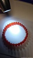 Photo of natural red carnelian bead stretchy bracelet illuminated by light, showing translucent red-orange beads arranged in a circle.