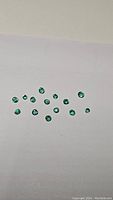 Photo of 21 small round natural emeralds on white background showing clarity and color.