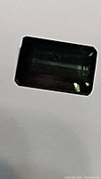 Close-up photo of a dark green octagonal cut tourmaline gemstone lying flat.