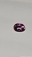 Close-up photo of oval cut natural hot pink topaz gemstone showing its intense pink color and faceting details.