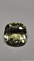 Close-up photo of natural lemon citrine gemstone showing cushion cut facets and light reflection.