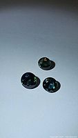 Three round cut green-blue sapphires displayed on a white surface showing color and reflective qualities.