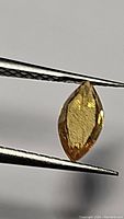 Close-up of golden yellow marquis cut natural sapphire held by tweezers showing facets and color.