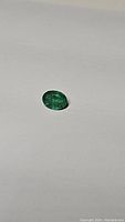 Front angled view of the oval cut Zambian emerald gemstone on a plain surface, showing its deep green color and size.