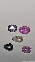 Five multicolored untreated no heat sapphires laid out on a plain surface, showing various cuts including oval, pear, and cushion.