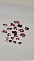 Photo of the parcel of 19 mixed cut pink tourmaline gemstones, showing range of colors from light to dark pink, some inclusions visible