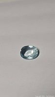Untreated oval cut aquamarine gemstone on neutral background, showing its color and cut.