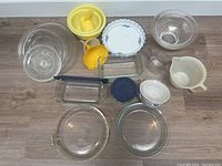 Photo showing a collection of various Pyrex and other kitchen glass and plastic bowls, baking dishes, measuring cups and kitchen tools arranged on the floor.