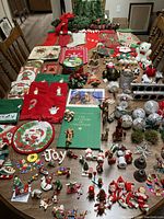 Full collection displayed on table showing wide variety of Christmas-themed items including ornaments, stockings, books, towels, trays, and cards.