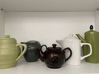 Front view of five collectible teapots arranged on shelf showing varied colors and shapes, in good condition
